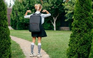 Young girl points to large heavy backpack she is wearing on first day back to school.