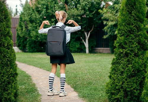 Young girl points to large heavy backpack she is wearing on first day back to school.